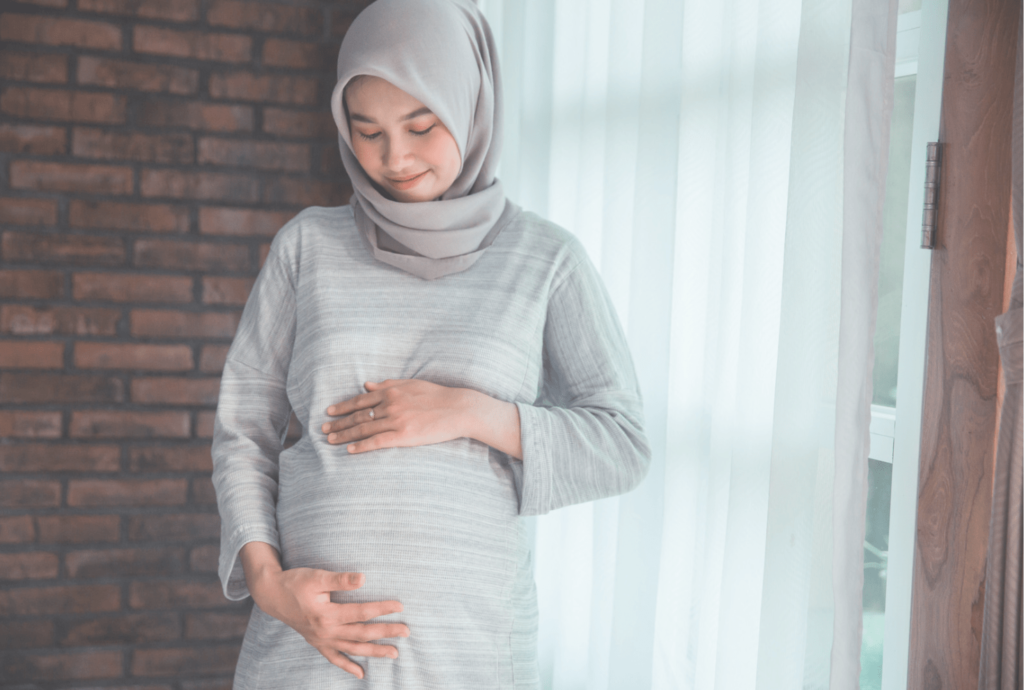 Pregnant woman leaning against wall and cradling stomach